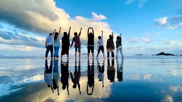 a group of people standing at the edge of the ocean with a blue sky