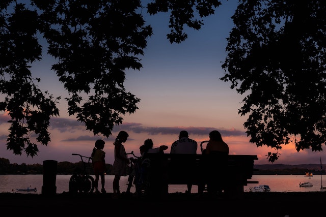 photo of 6 people of different ages sitting on a bench looking out a lake at sunset