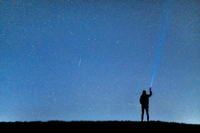 Silhouette of person shining a light up in to the stars in the sky 