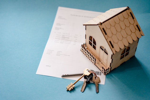 photo of a model wooden house sitting on a piece of a paper with a set of keys