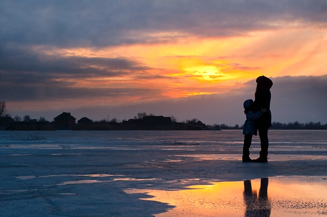 Child and Woman Standing Near Water at sunset