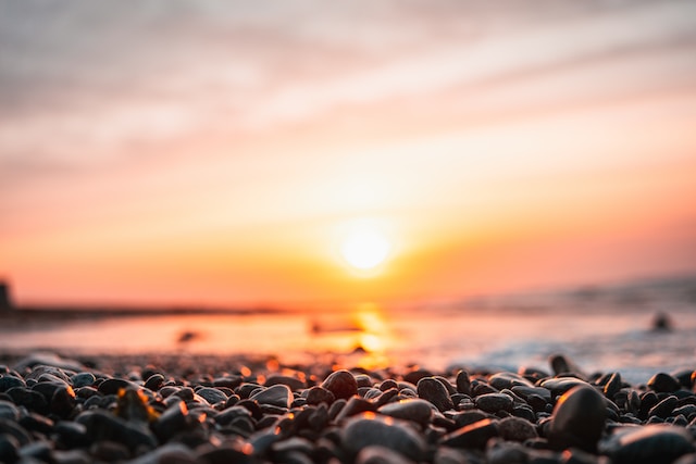 Photo of pebbles and the ocean with sunrise in the background
